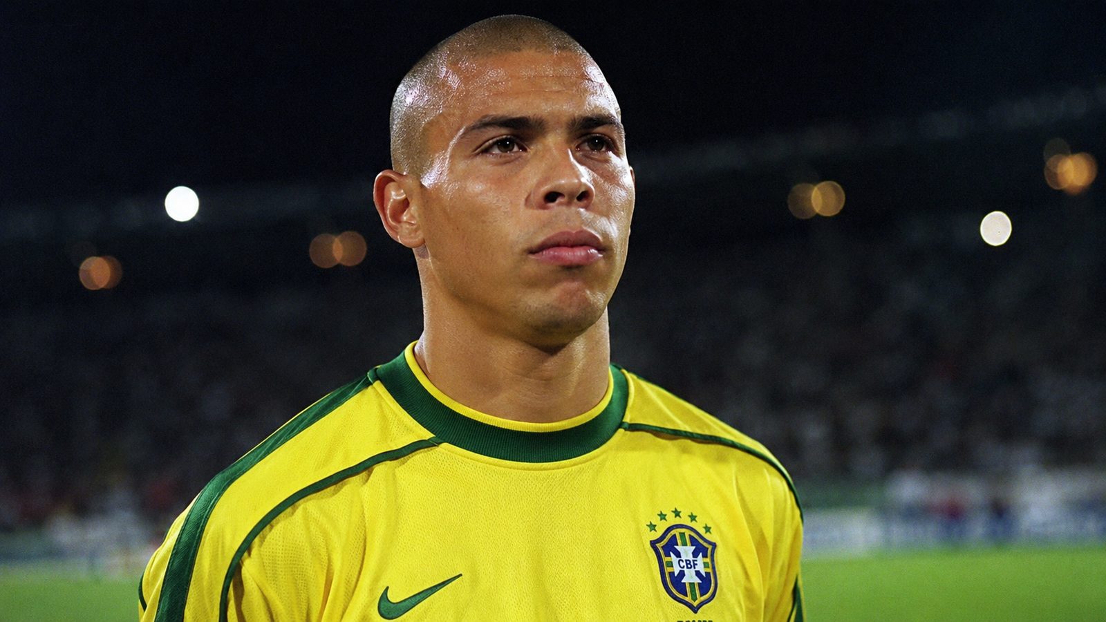 Ronaldo Nazário looks serious in a Brazil jersey under stadium lights, evoking the pressure surrounding the 1998 World Cup final.